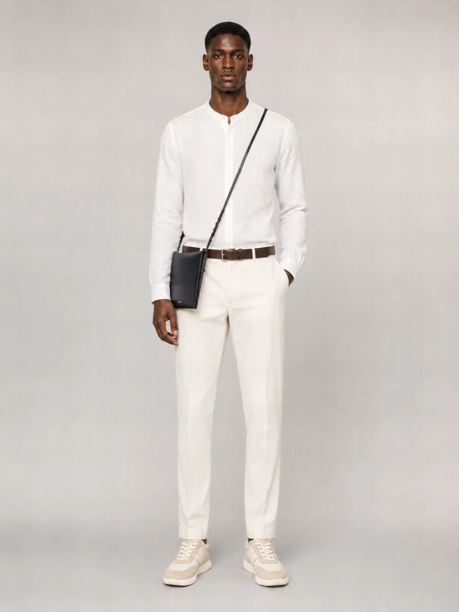 A soft white mandarin collar shirt and off white tailored trousers form a calm, precise base in pale neutrals. Off white and sand sneakers keep the energy relaxed but considered, while a dark brown belt and slim navy crossbody add just enough contrast and structure. The result is warm weather tailoring that reads modern, composed and easy to wear from daytime appointments to dinner.
