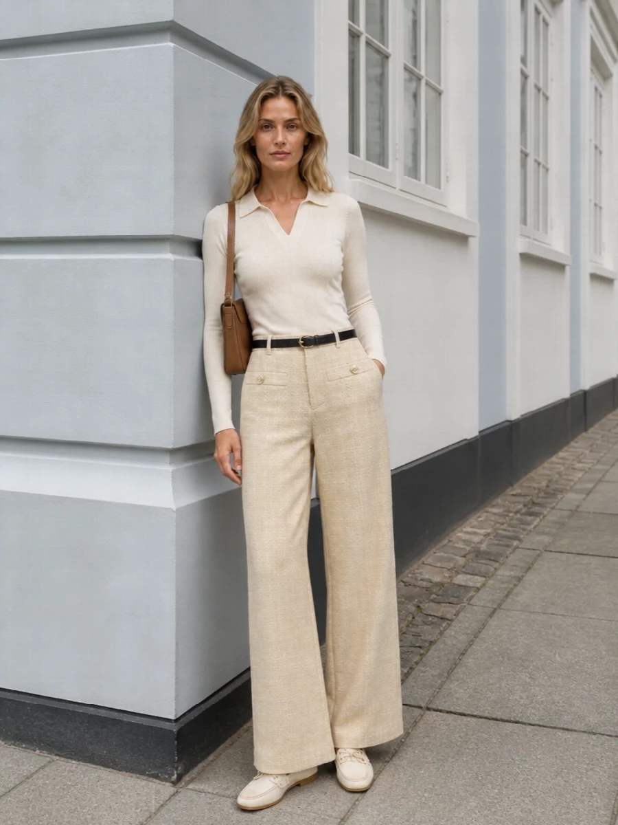 An ivory ribbed knit meets high-rise light beige wide legs for a clean, elongated line that feels polished without skewing formal. Off-white moccasin loafers keep it quietly preppy, while a tan camel shoulder bag and slim gold-detailed belt bring just enough structure and warmth. The result is a softly tailored neutral ensemble that moves easily from city mornings to late afternoon plans.