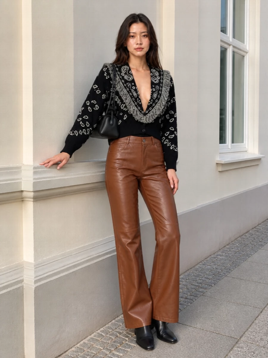 The bandana-fringed cardigan sits over caramel leather flares, giving a rich contrast of texture that still reads controlled and polished. Sleek black ankle boots lengthen the line, while the sculptural black shoulder bag quietly underlines the artistry. The result is a graphic, modern city outfit that moves easily from daytime errands to low-lit dinners without changing a piece.