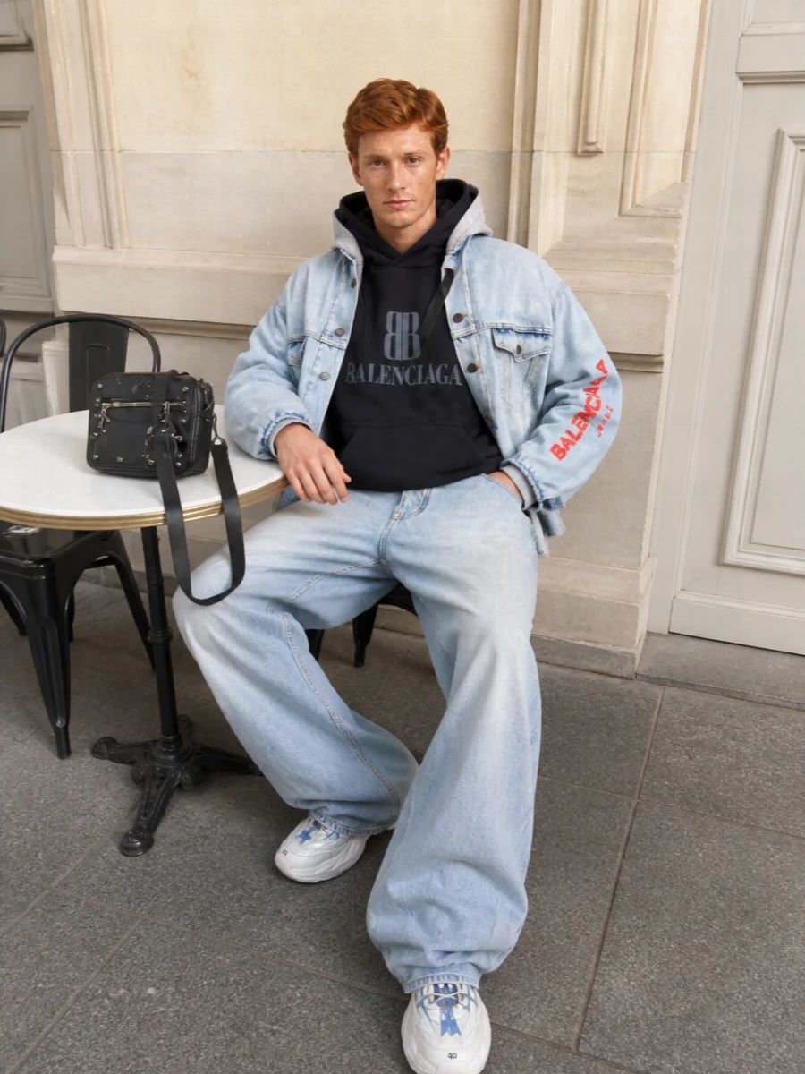 Head-to-toe Balenciaga denim and fleece keep this outfit firmly in that grunge-skate city lane, with washed blacks grounding the pale blue jacket and jeans. The ultra-wide leg and oversized hoodie play with volume while scuffed runners and a moto-influenced crossbody add that lived-in, backstage attitude. It is an easy uniform for cold urban days when you want the branding to read clearly but the palette to stay tight and wearable.