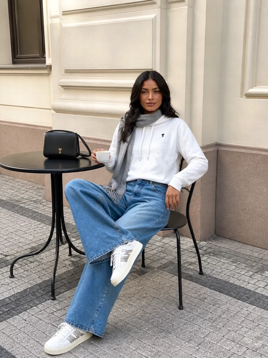 A cropped Ami hoodie sits cleanly over architectural wide-leg denim for a modern, relaxed silhouette. White Moncler sneakers and a structured black shoulder bag sharpen the palette without losing ease. A soft heather-grey scarf finishes the mix with a subtle layer of texture and warmth.