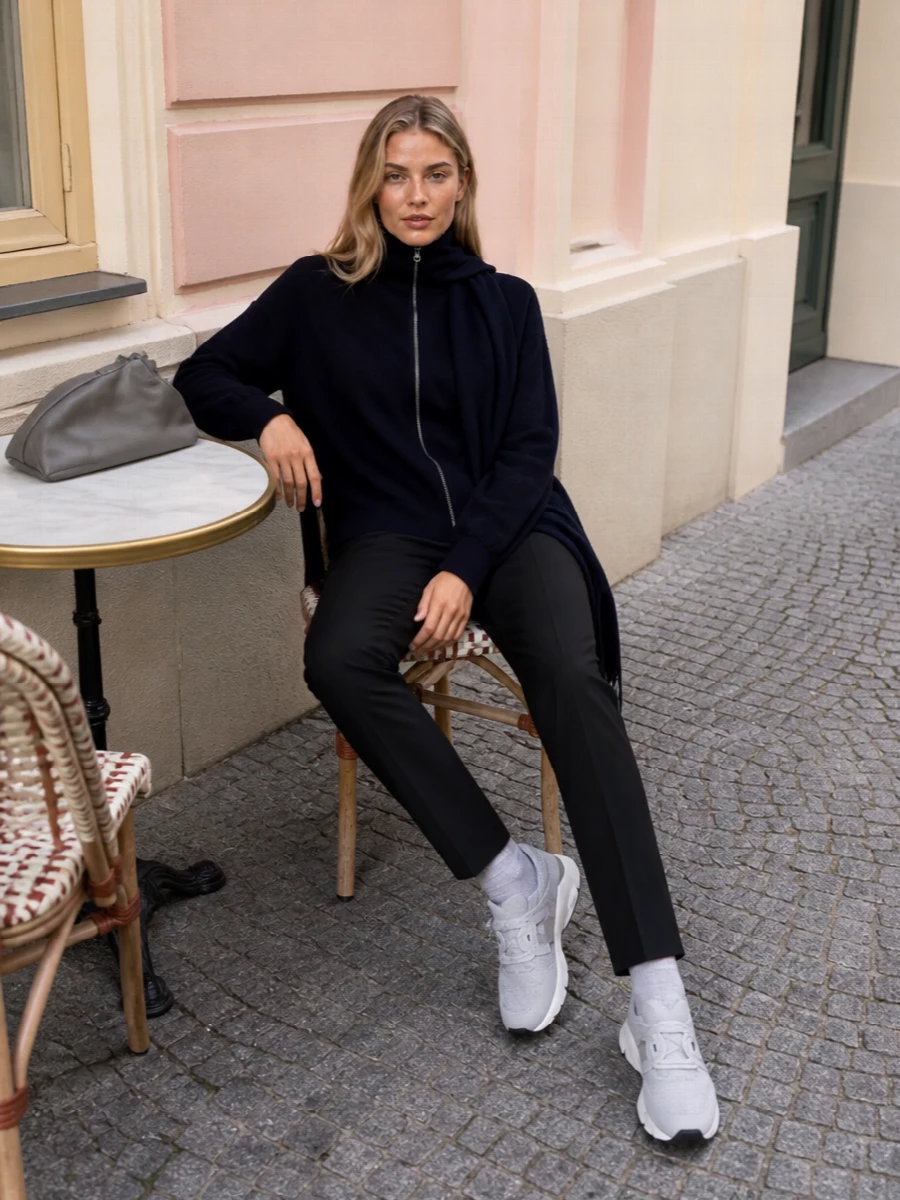 A navy funnel-zip knit meets softly structured black trousers for a quiet, modern uniform that moves easily from commute to low-key dinner. Light-grey sock sneakers and a steel-grey shoulder bag keep the mood calm and practical, adding just enough contrast without loud color. A matching ink scarf finishes the line, sharpening the high neck and keeping the silhouette long and unfussy.