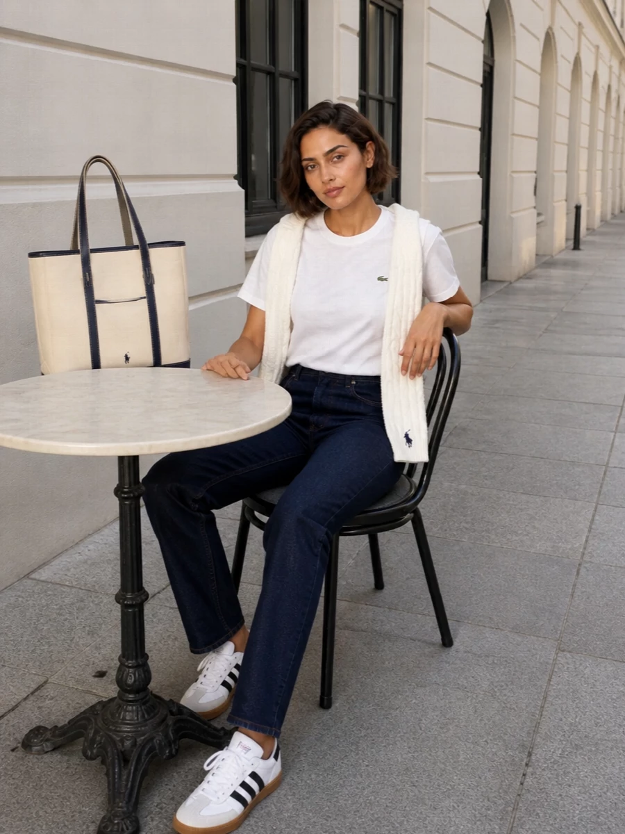 A clean Lacoste tee and dark indigo straight-leg denim form a quietly sporty, preppy base that works from campus to casual Fridays. Classic white-and-gum Adidas sneakers keep it grounded in sport heritage, while the sand-and-navy tote and soft cable scarf add just enough collegiate structure without feeling try-hard.