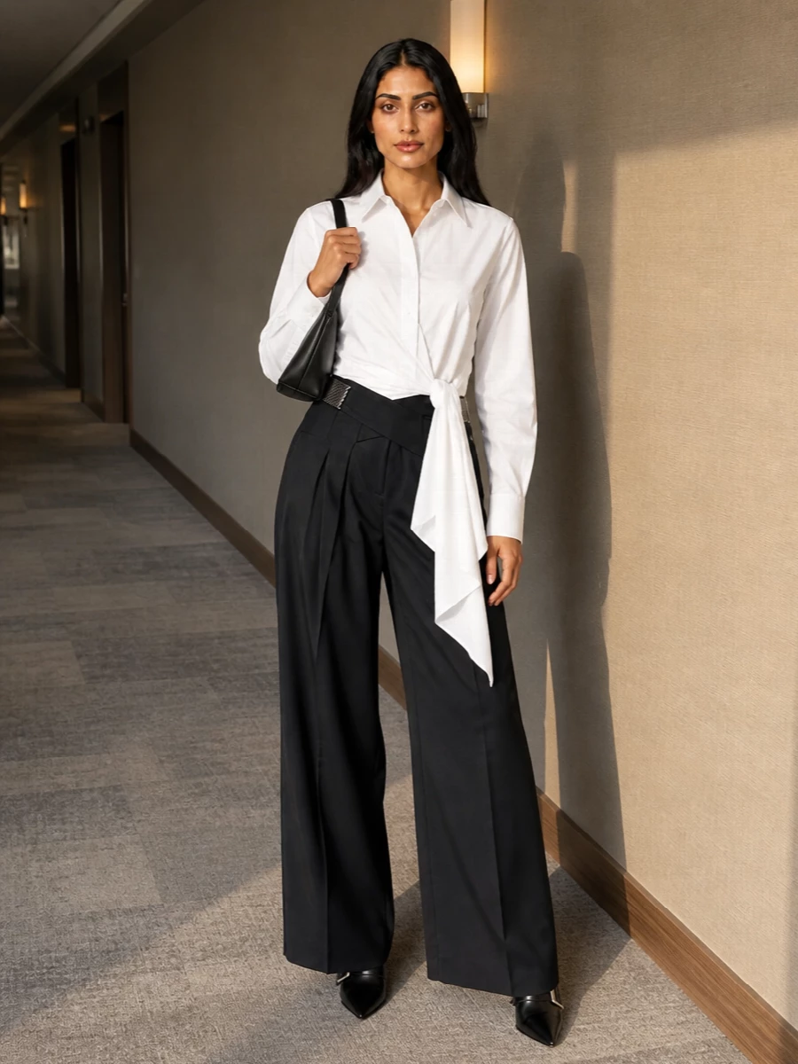 Attico’s charcoal wide-leg trouser meets its match in the crisp white tie-front shirt, the wrapped waist and sculpted sash creating a cinched, architectural column. Balenciaga’s razor-point ankle boots keep the proportions elongated and sharp, while The Attico’s triangular clutch quietly echoes the geometric lines. The result is modern evening tailoring that reads precise, minimal and confidently polished in deep neutrals.