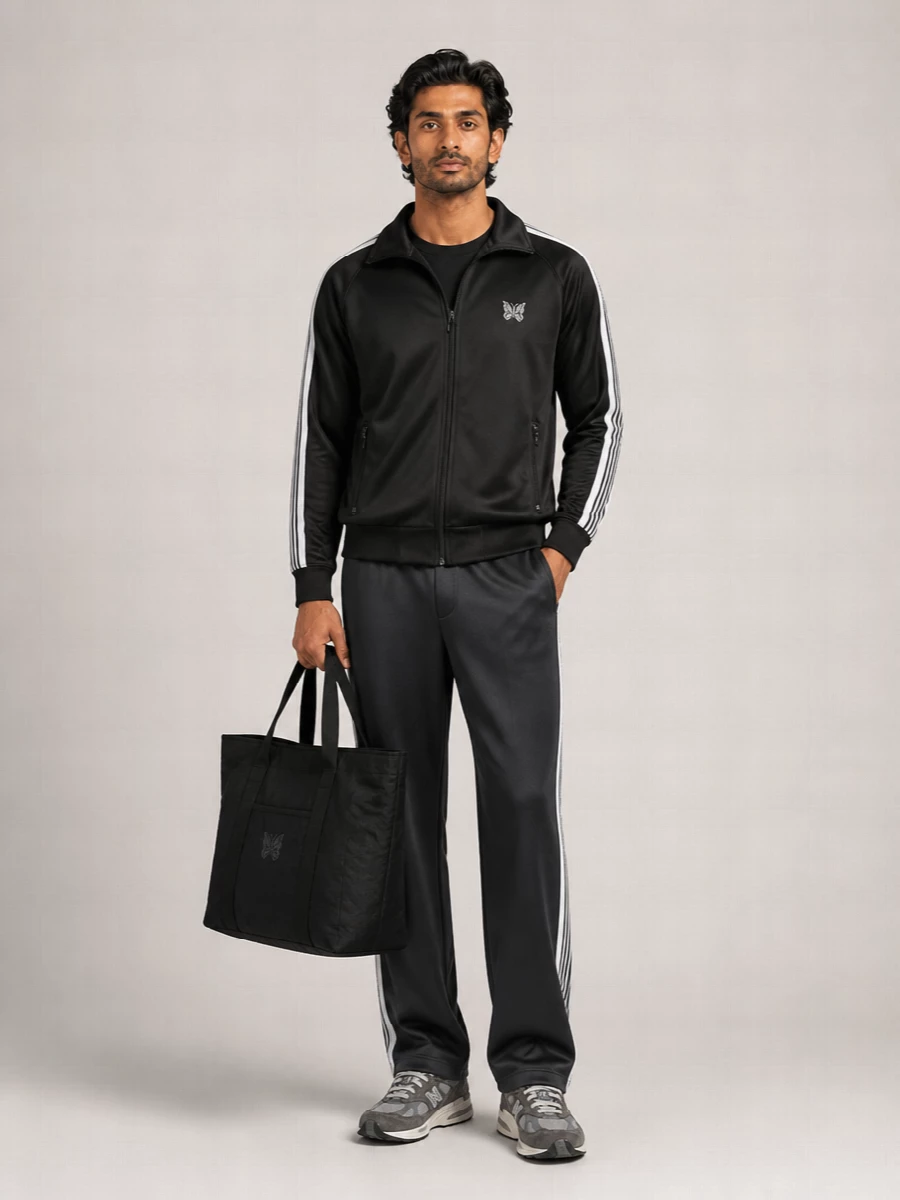 Needles’ track jacket sits over a matching charcoal track pant, turning sport detailing into a sharp, uniform-style street set. Grey New Balance runners and the oversized black butterfly tote keep everything in a tight monochrome story with just enough technical texture. It feels like a considered off-duty uniform that moves easily from commute to late-night city laps.