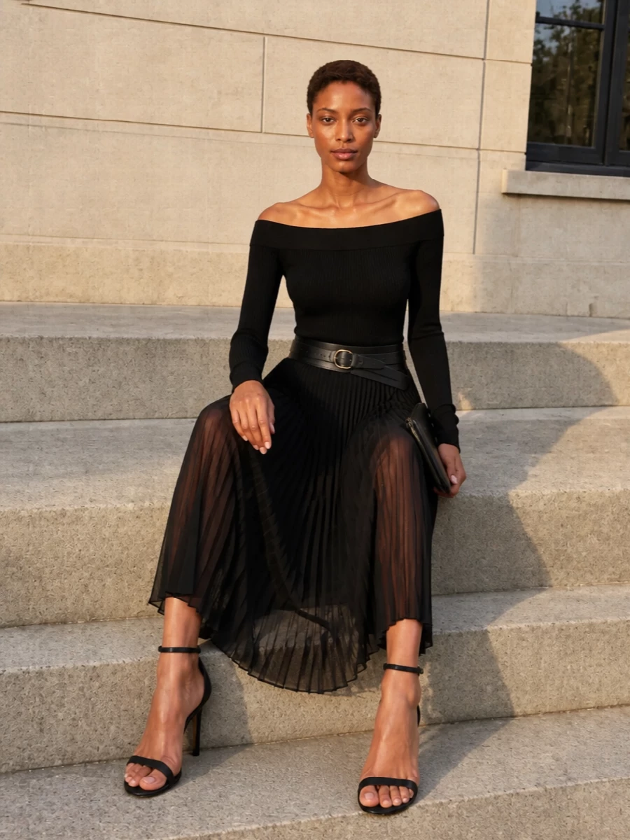 This is Alaïa at its most distilled: a sheer black pleated midi grounded by an off-the-shoulder second-skin knit for a precise, graphic evening line. A sculpted black waist belt turns the pairing into a single, cinched column, while razor-thin stiletto sandals and a slim black clutch keep everything rigorously minimal and quietly luxurious. It is an all-black composition that relies on proportion, texture and negative space rather than embellishment for impact.