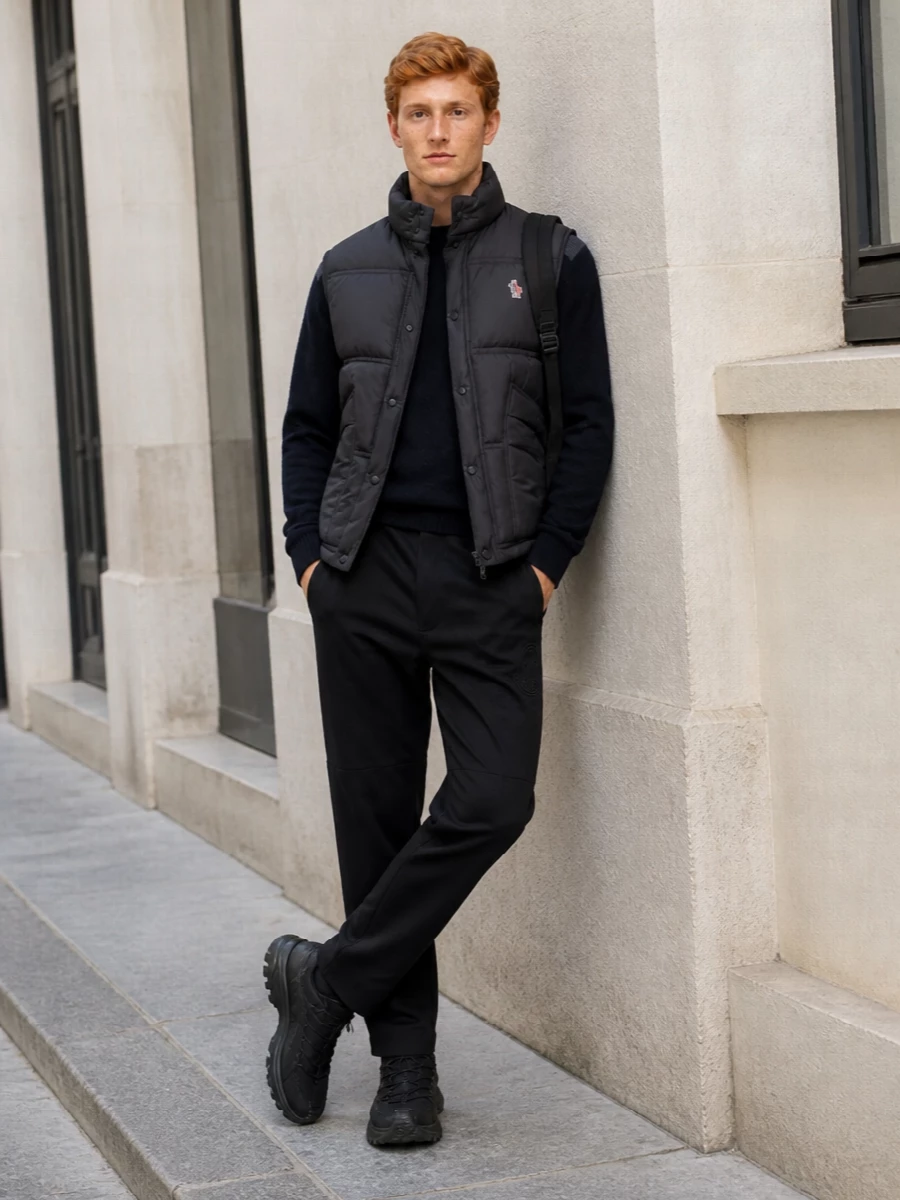 This look builds a sophisticated alpine-athleisure story around the charcoal Moncler Grenoble gilet, pairing it with a navy technical crew knit and clean black straight-leg trousers for a quietly luxurious winter silhouette. Chunky black trail sneakers and a sleek black Moncler backpack keep the line modern and functional, perfect for city commutes that can stretch into mountain weekends without a change of gear. The palette stays tightly controlled in charcoal, navy and black, letting texture and technical detailing do the talking.