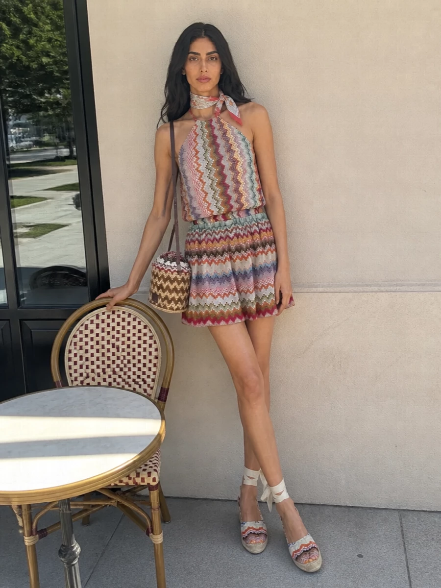 A head-to-toe Missoni moment, grounded with raffia textures, turns this halter mini into an easy holiday statement. Chevron espadrille wedges keep the lines elongated, while the woven bucket bag and sun-washed paisley neckerchief add just enough boho detail. It is made for beach clubs, terrace lunches and rooftop cocktails where colour and print feel completely at ease.