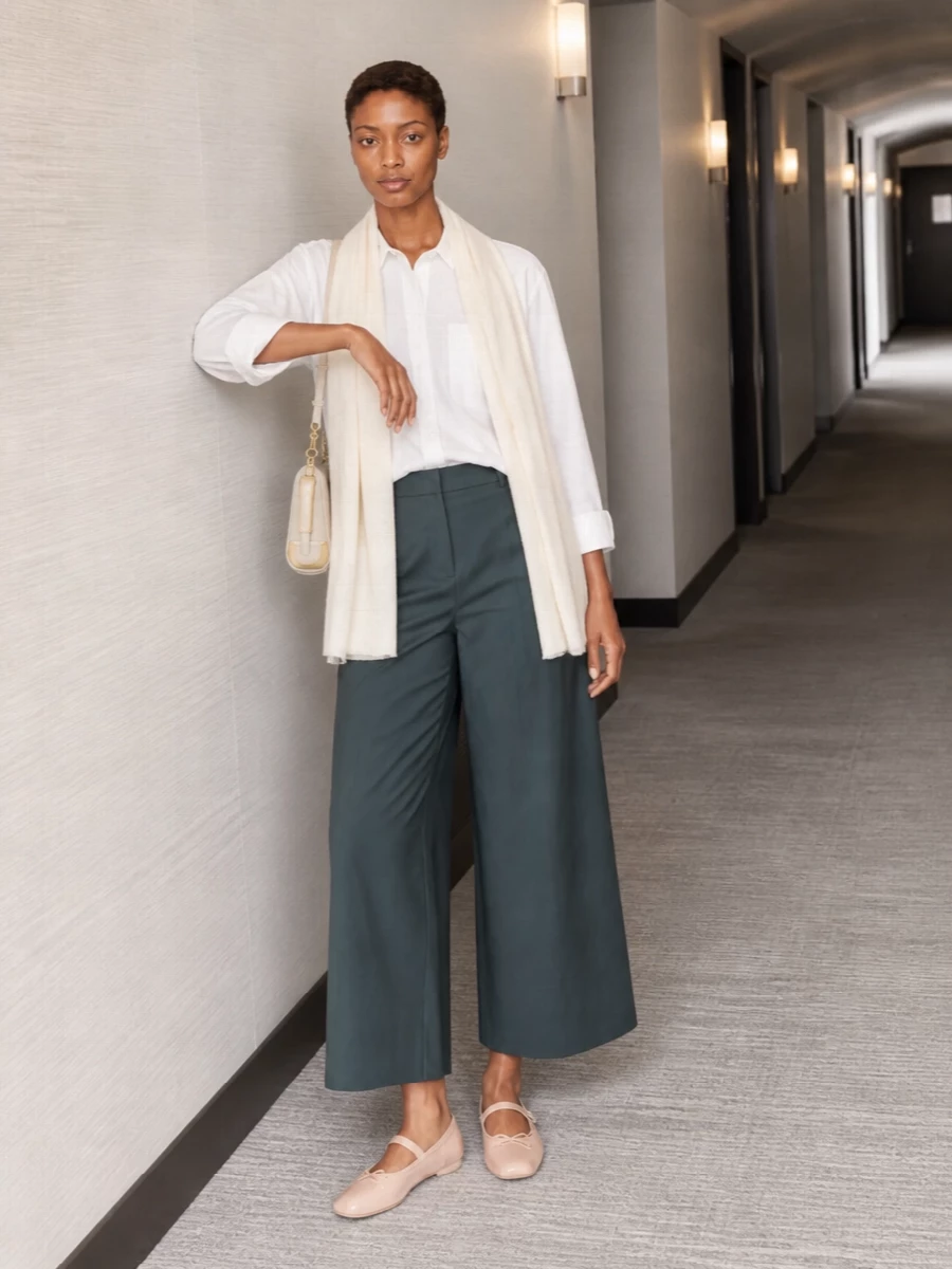 Slate teal wide-leg trousers are grounded with a relaxed white shirt for a clean, airy take on weekday minimalism. Nude-hued ballet flats and a cream shoulder bag keep the palette soft and refined. An ivory scarf ties the neutrals together, adding just enough texture without disturbing the quiet ease.