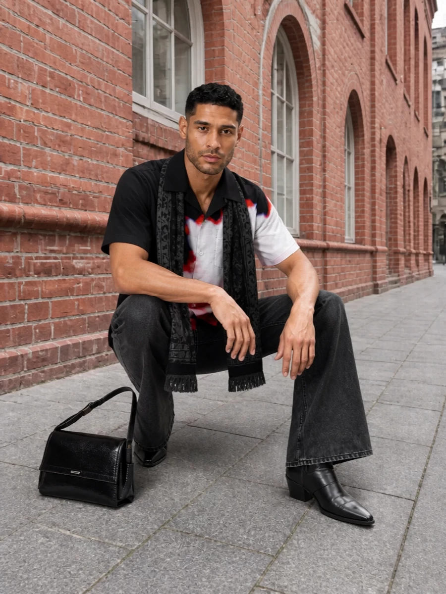 A bold McQueen floral shirt meets washed black flared denim for a sharp, street-tailored silhouette that feels built for night. Pointed black boots extend the line and add rock tension, while a structured black shoulder bag keeps the finish polished and graphic. The result is a clean monochrome base that lets the scarlet and off white print do all the talking.