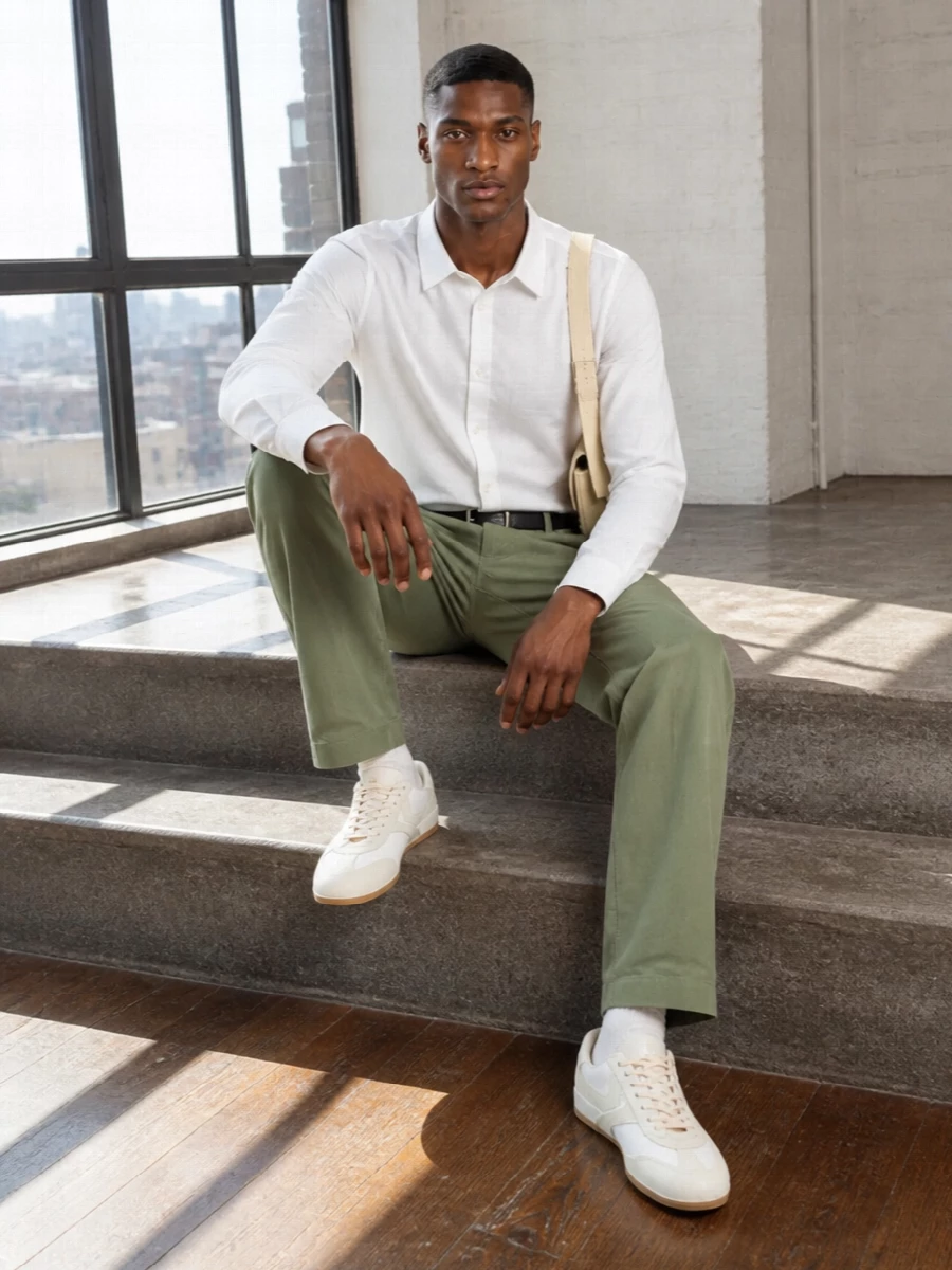Sage straight-leg trousers meet a razor-clean white shirt for a calm, precise take on warm weather dressing. Off-white retro runners and a buttercream shoulder bag keep everything light, while a slim black belt adds quiet definition. The result is polished enough for lunch in the city yet relaxed enough to move easily through the day.