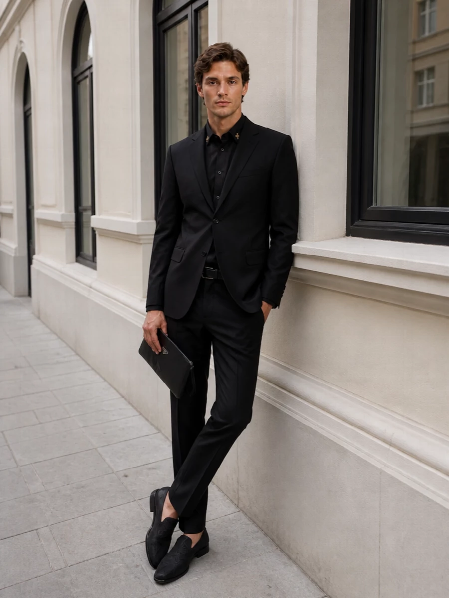 A razor-sharp black trouser grounds the embroidered shirt in pure Italian evening polish, keeping the line long and lean. Brocade loafers echo the shirt’s quiet opulence while the minimal wristlet and belt keep the mood disciplined rather than flashy. It is a confident, monochrome answer to dinners and late-night rooms where subtle detail matters more than shine.