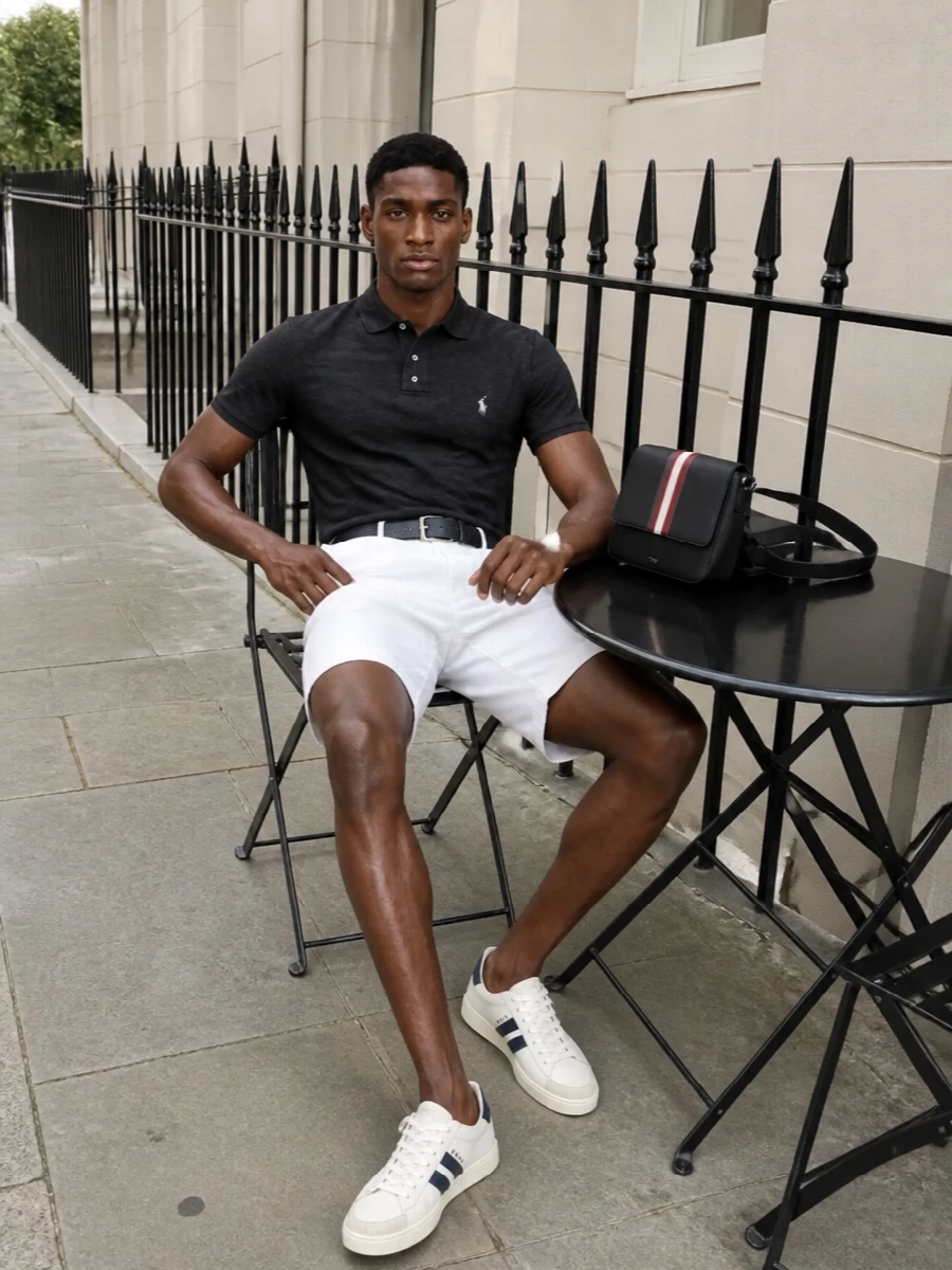 Charcoal piqué against optic white creates a sharp, collegiate contrast that feels easy for warm days yet still put together. Off-white and navy court sneakers keep the line relaxed but refined, while a slim navy belt and structured crossbody quietly pull everything into one clear preppy story. It is a clean, modern way to wear Polo that moves from terrace lunches to casual evenings without changing a piece.