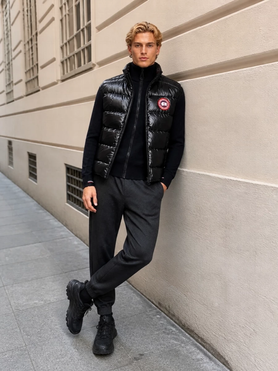 A high-gloss Canada Goose gilet tops a quietly technical base, all in deep blacks and charcoals that feel sharp rather than sporty-casual. The tapered Givenchy joggers and Moncler trail runners keep the profile agile, while the streamlined backpack locks everything into a cohesive, city-ready winter uniform. It is performance gear styled with luxury discipline, ideal from airport gates to cold urban commutes.
