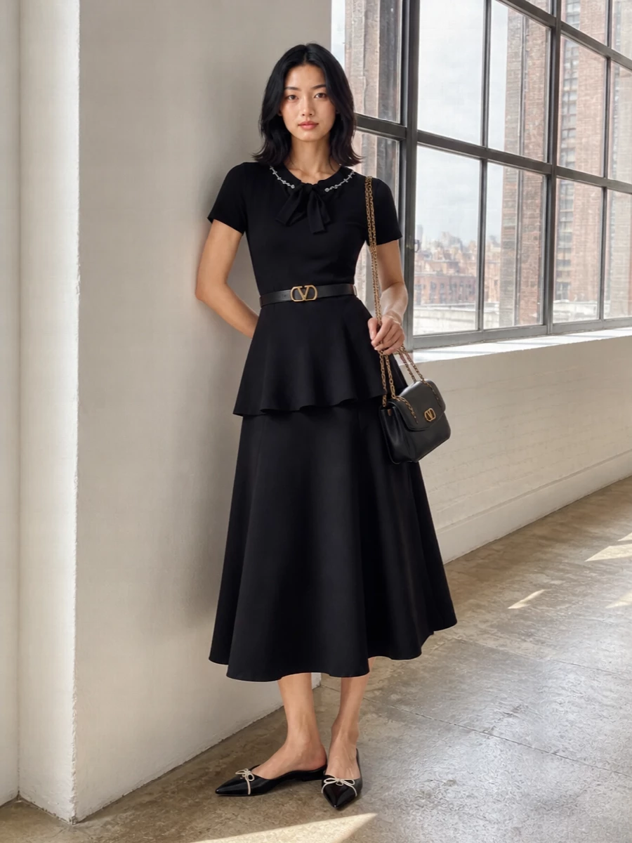 A monochrome play of volume and precision, this pairing turns the embellished knit tunic into a modern, dress-like silhouette over a sculpted black flared skirt. Pointed flats keep it quietly formal yet wearable, while a chain-detailed shoulder bag and fine belt bring just enough gold to echo the jeweled collar without competing with it. The result is romantic, city-ready polish that moves easily from daytime engagements to intimate dinners.