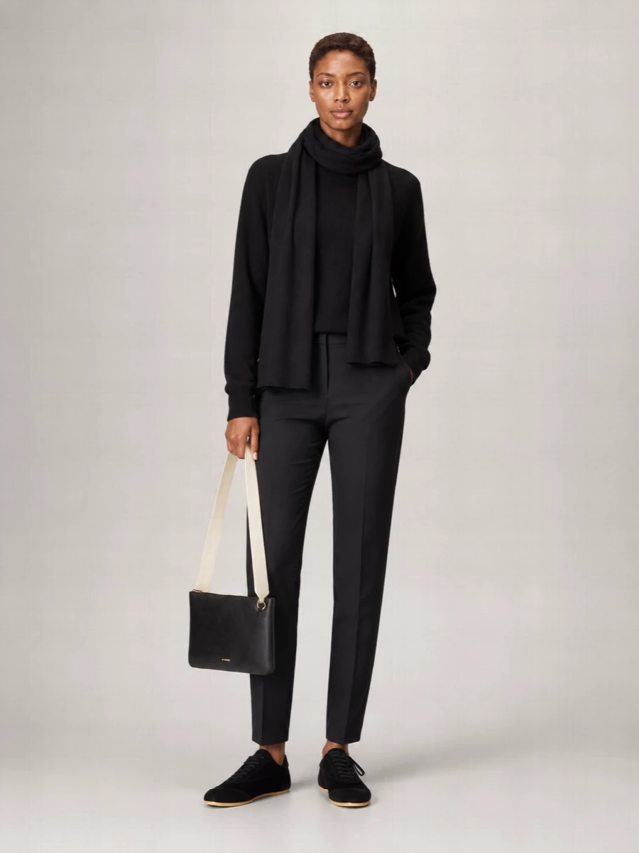 A black cashmere crew and matching tailored trousers create a calm, monochrome column that works from commute to late dinner. Sleek black sneakers keep everything grounded but relaxed, while a sharply minimal shoulder bag and long black scarf add quiet structure. The result is a low-key, modern uniform that reads considered without ever feeling dressed up.