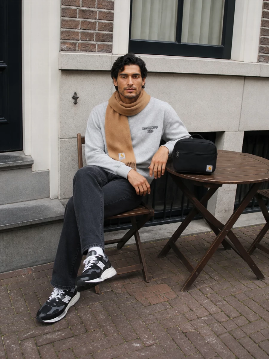 Light grey fleece on top and washed black denim on the bottom keep the outfit clean, easy and grounded in Carhartt’s utility street language. The technical New Balance runners add subtle performance energy, while the compact crossbody and camel scarf introduce just enough function and warmth without breaking the minimalist rhythm.