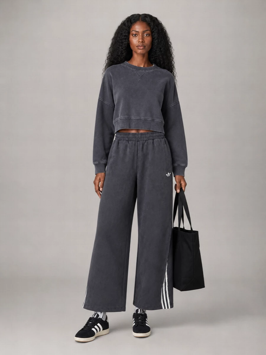 A washed-charcoal crop with high-rise wide legs creates an easy, monochrome column that still feels sharp and intentional. Low-profile black sneakers and a clean black tote keep everything graphic and agile rather than bulky. Striped sport socks introduce just enough logo detail to underline the athletic mood without breaking the minimalist palette.