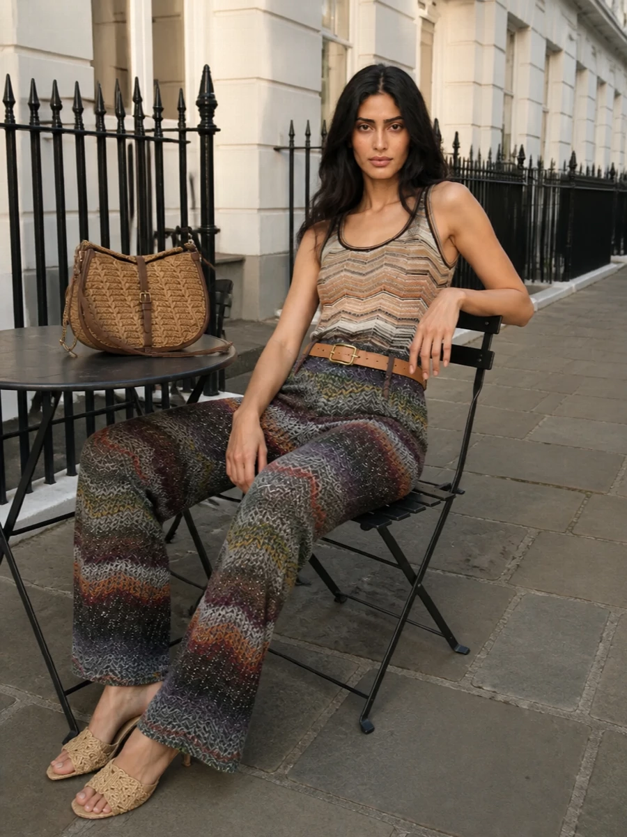 Missoni’s chevron knit trouser is grounded with a sun-faded neutral tank that lets the rich slate, taupe and forest tones stay in focus. A slim tan belt and woven Bottega mules sharpen the wide-leg proportion and keep everything light for warm evenings. A curved Etro shoulder bag in tan and chocolate finishes the outfit with textured, quietly decadent polish that still feels relaxed and bohemian.