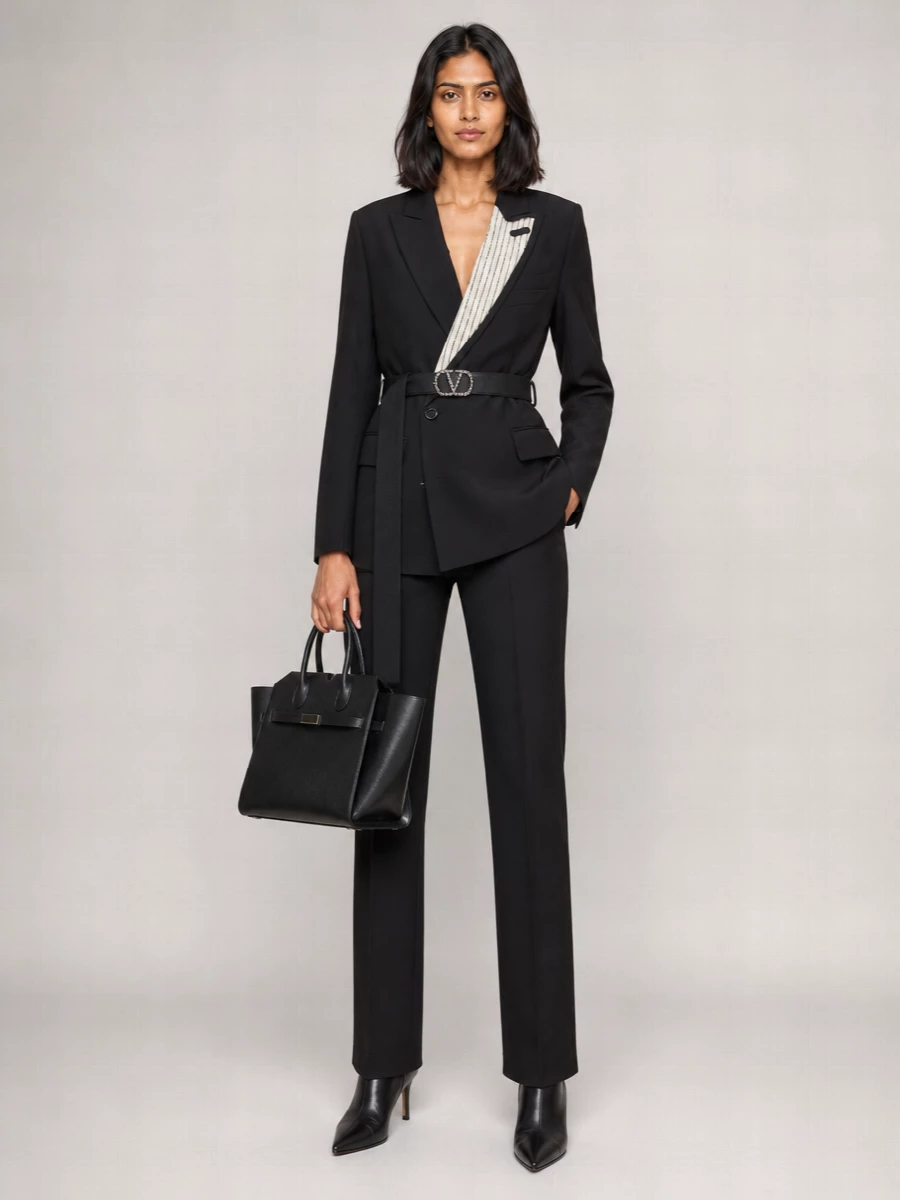 A sharply tailored black blazer mini is grounded with straight-leg suiting trousers and knife-point ankle boots for a long, city-ready line. The structured black bag and crystal-detailed belt keep the mood quietly glamorous, ideal for evenings when you want polish with a modern edge.