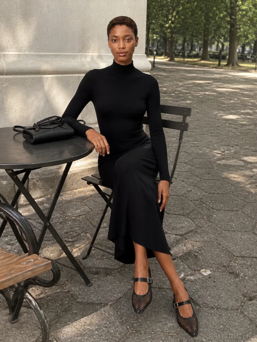 The Alaïa knit midi dress and mesh Mary Janes create a continuous, inky column that feels precise yet quietly sensual, with the heart-shaped back cut-out echoing the subtle reveal of the shoe. The ribbed knit, pointed toe and block heel all speak the same architectural language, while the slim black clutch keeps the focus on line and movement for gallery nights or intimate dinners. Choosing the dress route over separates keeps the story pure and modern, letting texture and cut carry all the drama in a single gesture.