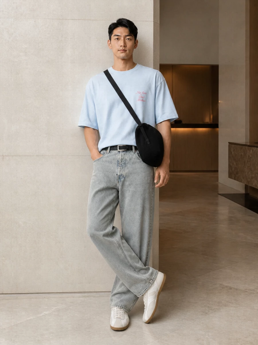 Faded straight-leg denim meets a soft, oversized ice-blue tee for a laid-back, low-contrast palette that feels easy and graphic at once. Off-white retro trainers keep the line light and streamlined, so the jeans still read relaxed without feeling heavy. A sculptural black crossbody and slim black belt add just enough structure to keep the whole outfit intentional, not sloppy, while staying firmly in that minimalist streetwear space.