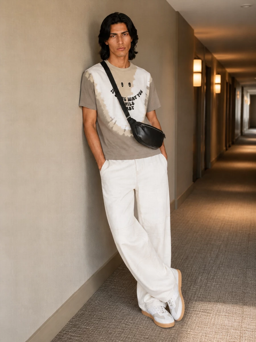 Mm6’s smiley tie dye tee sits over washed off white wide legs for a slouchy, sun‑bleached kind of streetwear. Soft taupes and chalky neutrals run from top to toe, with gum‑soled sneakers and a padded black crossbody adding just enough contrast. The result is relaxed but intentional, perfect for coffee runs, galleries and late summer evenings in the city.