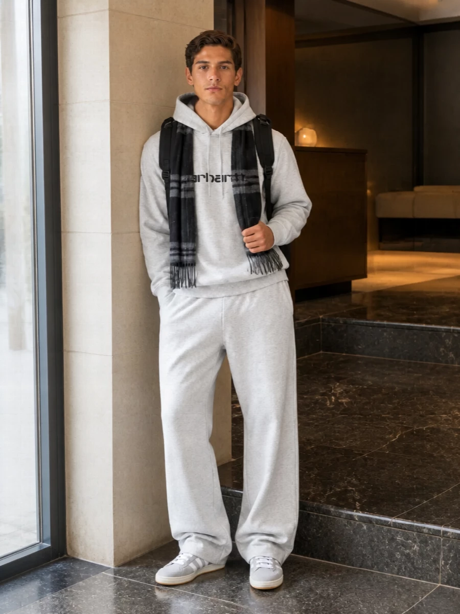 A heather grey Carhartt WIP hoodie and wide-leg sweatpant read like a considered city uniform, all in one soft tonal story. The relaxed fits stack neatly over the low-profile grey Campus sneakers, keeping the volume up top and through the leg but clean around the foot. A black backpack and charcoal toned scarf sharpen the palette just enough for streets and commutes without losing that off duty ease.