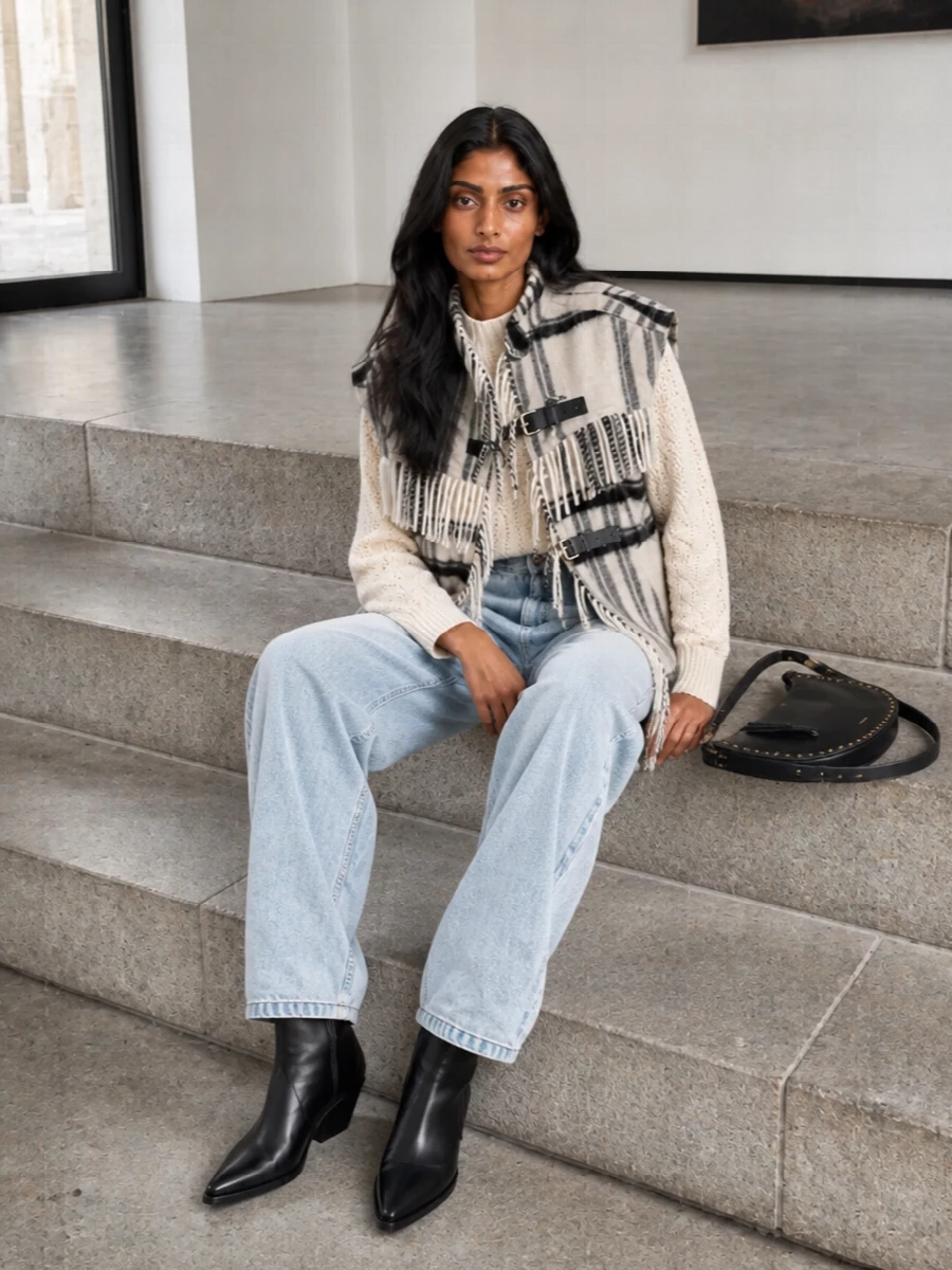 I am building around the vest as the anchor, so I skip dresses and keep to a knit and denim story that mirrors the original styling note. The cream cable sweater and high-waist light denim keep the palette soft and wintery, letting the checked fringe vest stay the statement while the black western boots and studded hobo quietly pull the darker accents through. The result is relaxed city-ready Isabel Marant energy, equal parts cozy and directional for cold-season days and casual evenings.