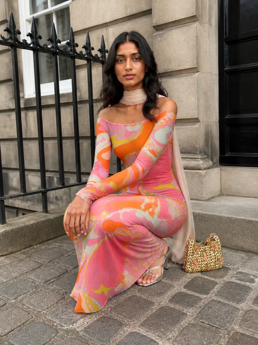 A vivid Pucci maxi becomes the star, grounded by sleek silver sandals and a jewel-like gold and blush mini bag. Metallic accents echo the dress’s light-catching energy while the soft nude scarf keeps everything feeling sensual rather than busy. The result is a high-summer evening ensemble that reads polished, playful and unmistakably glamorous from gallery hour to late-night terraces.