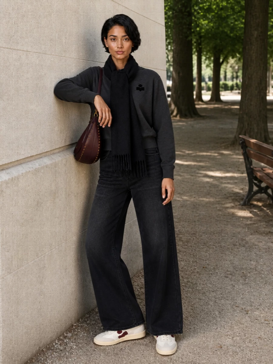 Charcoal tones stay tight from sweatshirt to wide-leg denim, giving a clean vertical line that feels relaxed but intentional. Off-white and burgundy sneakers with a matching crescent bag break the darkness just enough, keeping the palette graphic rather than flat. A simple black scarf finishes it with soft texture that suits cold city days without cluttering the silhouette.