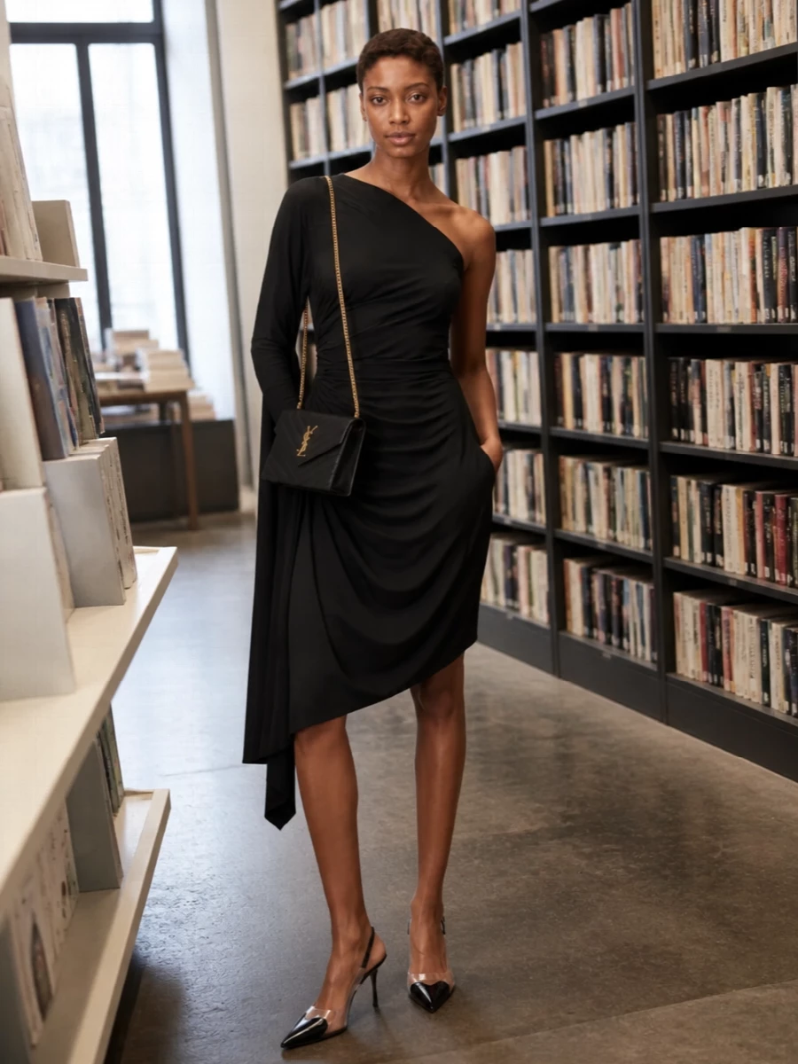 This is a pure evening moment built around sculpted black and clean hardware. The draped one-shoulder mini and knife-point slingbacks create a long, lean line that lets the Saint Laurent envelope bag read as the precise, gleaming accent. Choosing the dress route keeps the story minimal and focused, which suits the bag’s quiet luxury and high-formality energy far better than a separate top and skirt.