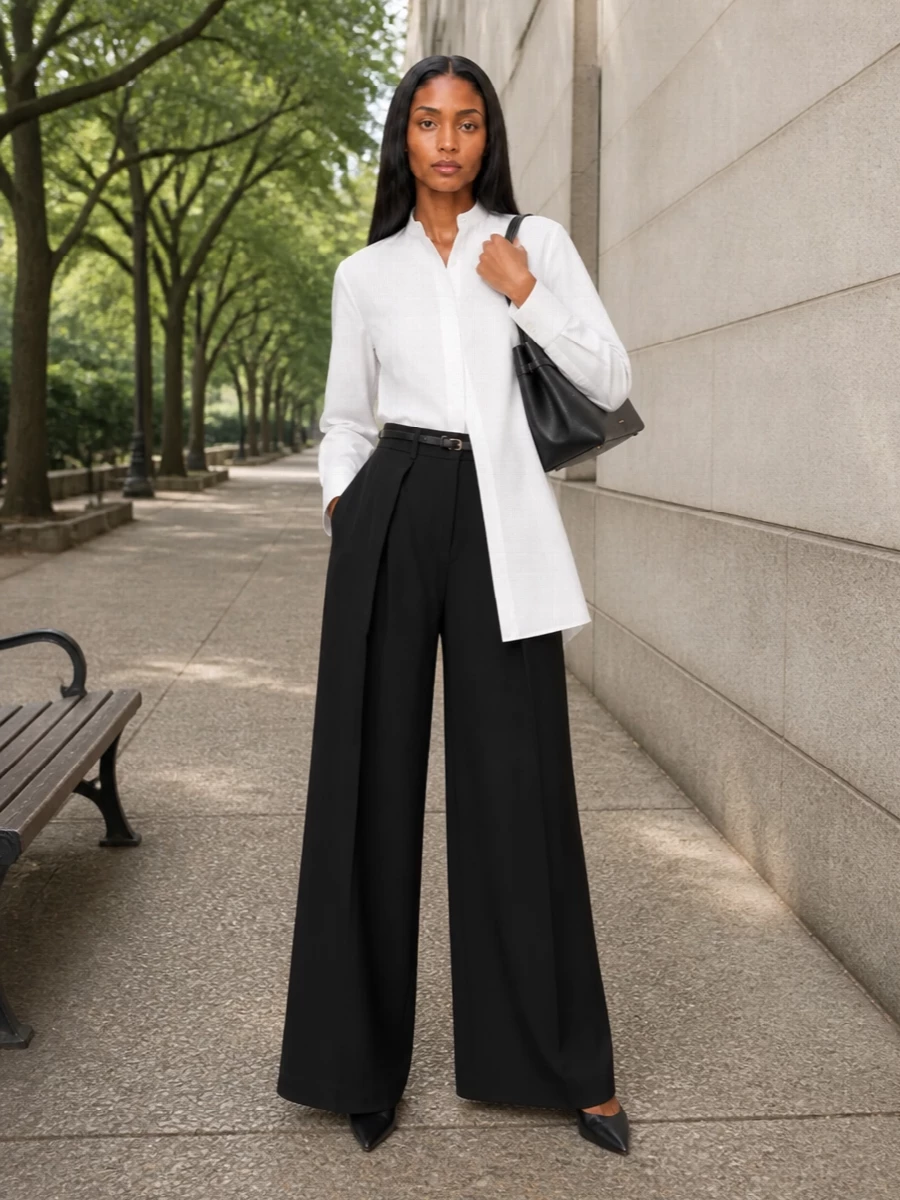 A sharply defined high-rise black trouser is paired with a longline white shirt for a graphic, elongated column that feels precise yet understated. The pointed black slingback and structured top-handle bag keep the silhouette clean and formal, while a slim belt quietly articulates the waist. It reads as modern executive tailoring, composed and minimal from boardroom to dinner.