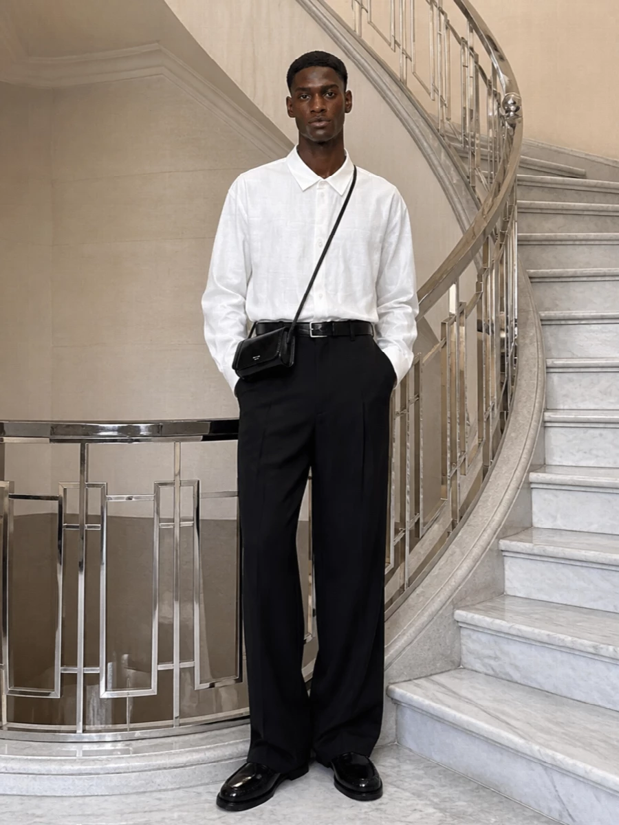 A Loewe wide-leg trouser with an oversized white shirt creates a precise, monochrome column that feels formal but quietly relaxed. Prada loafers and a slim crossbody refine the line without adding weight, while a sharp black belt gives just enough definition at the waist. It is an evening-ready uniform that reads considered, not fussy.