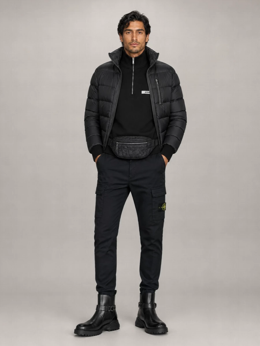 A cropped, padded Rick Owens bomber sits over a black Jacquemus half zip and tapered Stone Island cargos for a monochrome, utilitarian city uniform. Dior combat boots and a Valentino belt bag finish the outfit with polished toughness that stays firmly in the minimalist, street-driven lane.