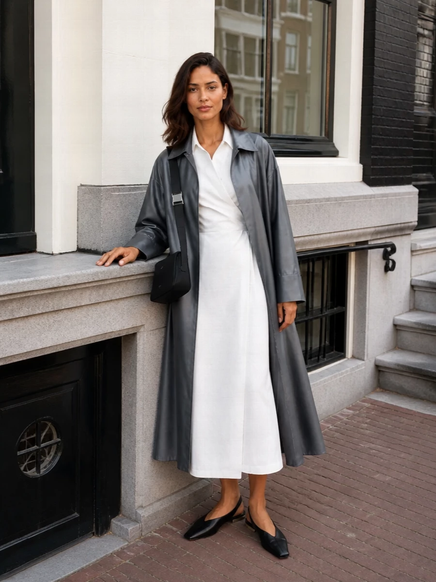 I am building around the coat and a dress rather than tailoring separates, because the trench wants a single clean column beneath it rather than competing lapels and layers. The Max Mara white wrap shirt dress, black slingback flats and compact black crossbody create a quiet grey–white–black palette that feels precise and long-lined, ideal for warm weather meetings or gallery evenings. The result is sharp but not severe, with the trench adding movement over a structured, minimal core.