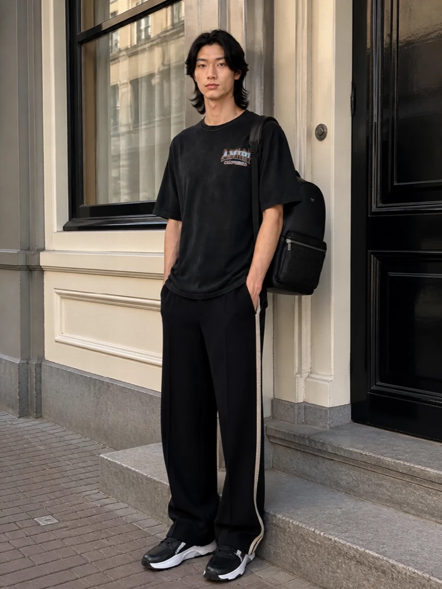 Amiri’s washed black graphic tee sits against equally relaxed Palm Angels wide-leg trousers, keeping the mood pure LA street in a clean dark palette. Chunky Fendi sneakers add a sharp, athletic base while the Jimmy Choo backpack brings practical edge without shouting over the flames on the chest. The result is a loose, stacked silhouette that feels confident but unfussy for city days and late nights alike.