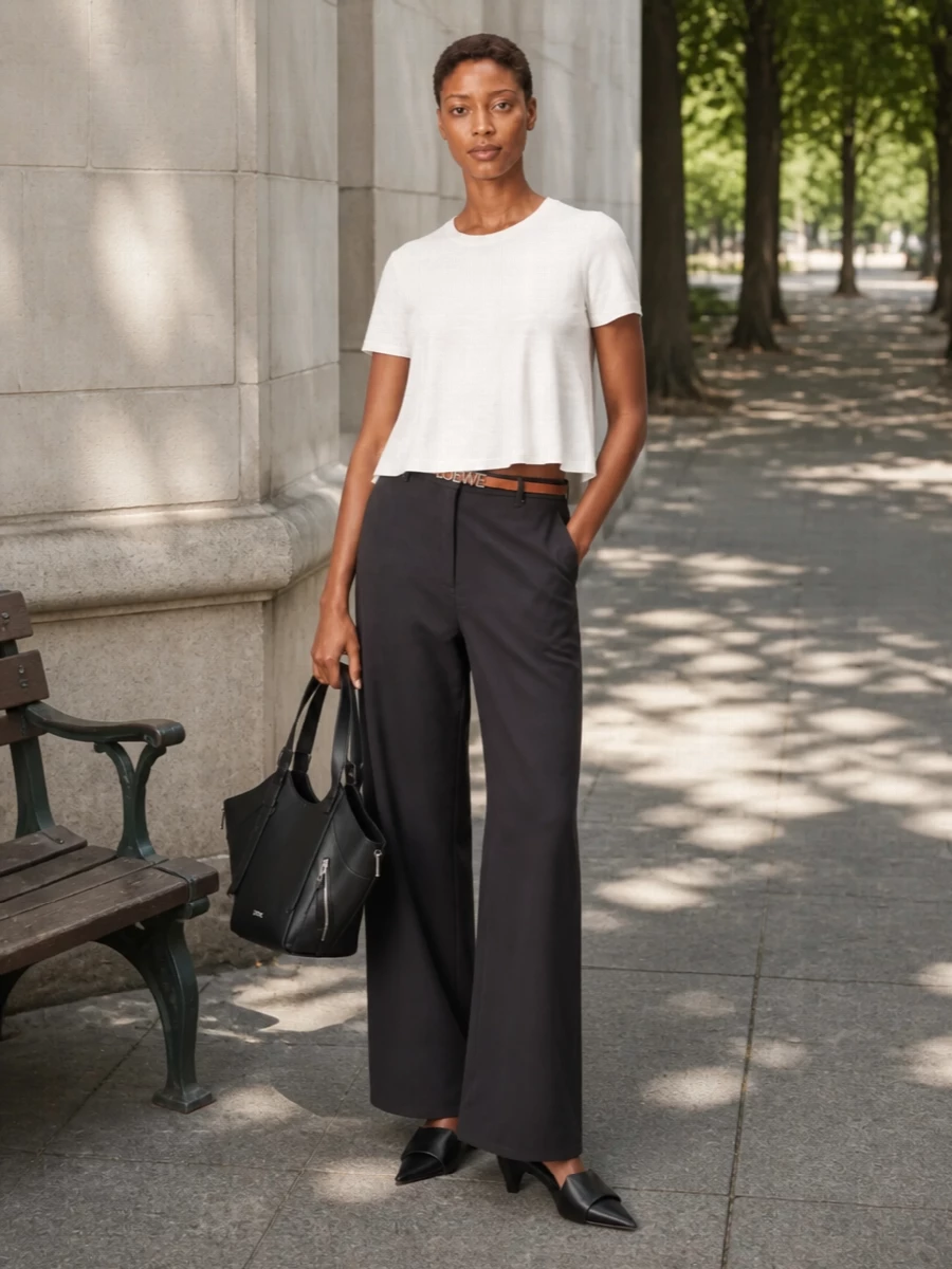 Loewe’s flared white tee and high-waisted black wide-leg trouser form a sculpted, monochrome column that feels clean, modern and quietly confident. Pointed black mules sharpen the proportions, while the structured black tote keeps the mood tailored and purposeful. A slim tan belt adds just enough warmth at the waist without disturbing the minimalist palette.