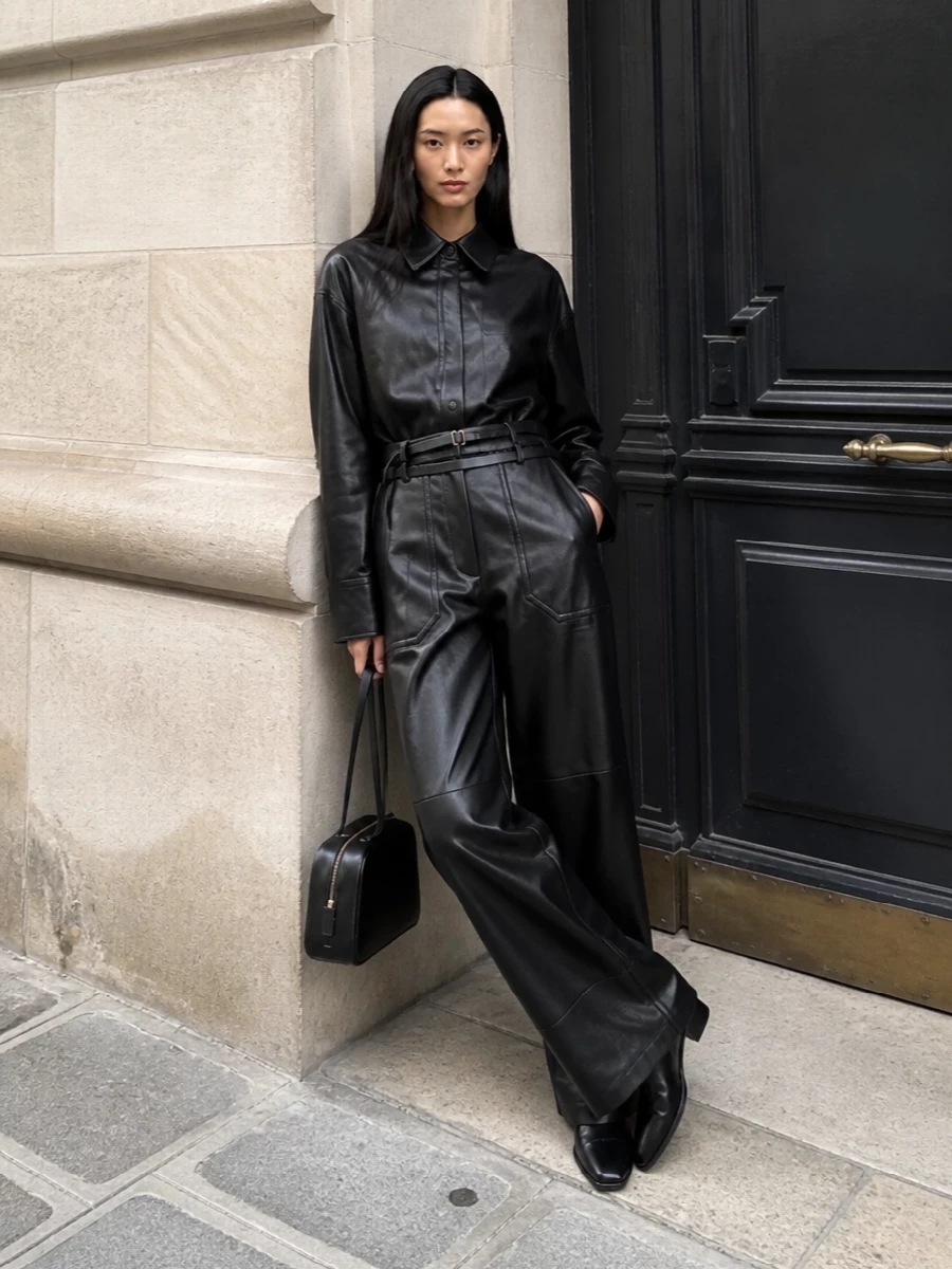 This look builds a sharp black column around the coated Sportmax shirt and matching wide-leg trouser, leaning into a minimalist, FW-appropriate take on modern power dressing. The Row sock boots keep the silhouette uninterrupted and elongated, while Khaite’s pared-back shoulder bag and a slim Bottega belt add just enough refined detail to underline the quiet-luxury attitude without disturbing the clean geometry.