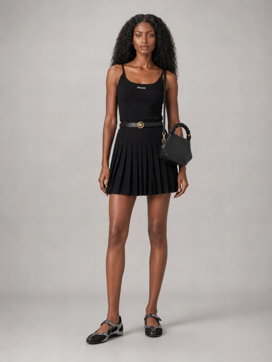 A black-on-black Versace set built for city pavement: sporty mini, sleek mesh sneakers and a compact cross-body that keeps everything light and fast. Gold hits stay precise at the waist, ears and bag, so the focus is the movement of the pleats and the clean athletic lines. It reads relaxed yet considered, ideal for days that flow from errands to low-key drinks without a shoe change.