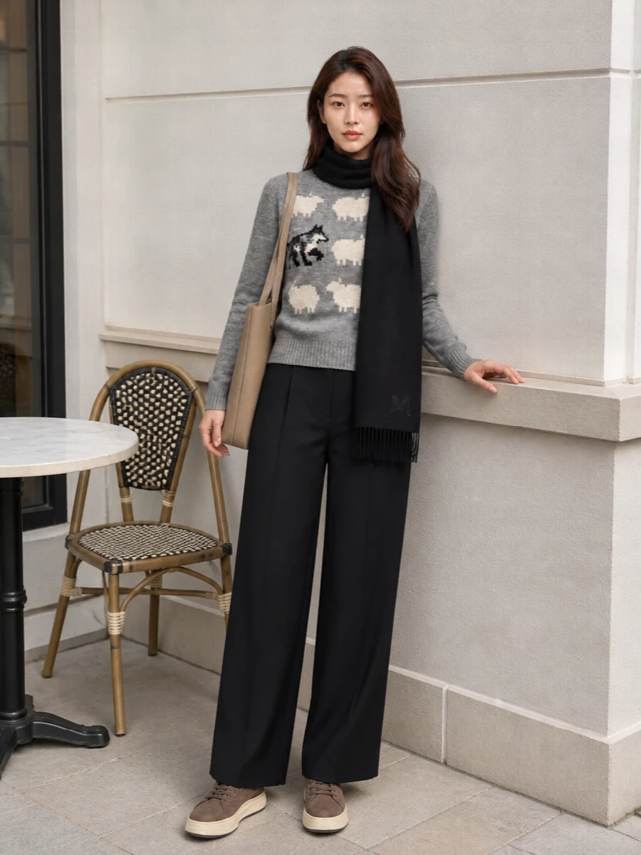 Graphic knitwear sits on sharp black wide-leg tailoring for a mix that feels relaxed but considered. Chunky taupe sneakers and a structured taupe tote soften the monochrome base while keeping it practical for city days. A simple black scarf ties the darker tones together and reinforces the quietly polished mood.