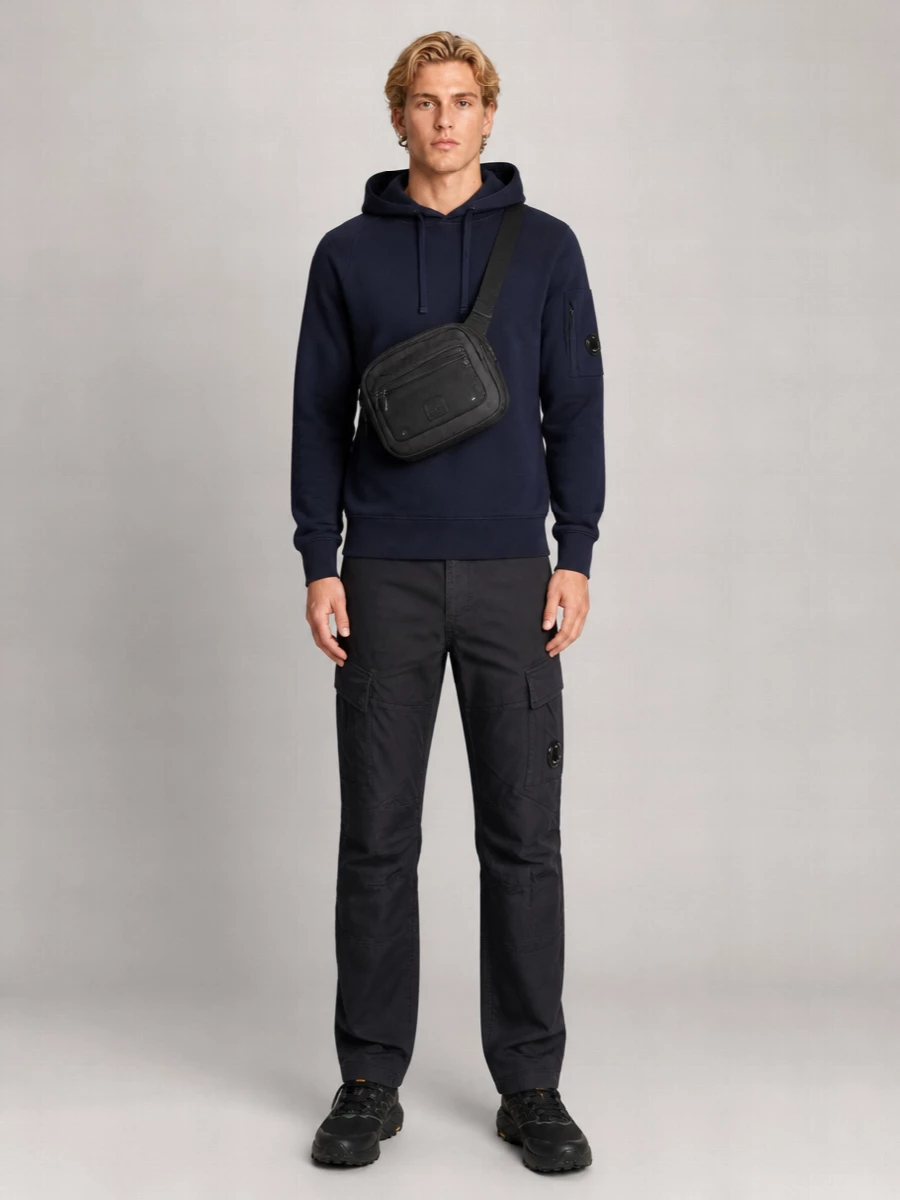 A navy-on-charcoal C.P. Company uniform that leans into technical utility without feeling overworked. The clean crew and straight cargos create a streamlined base, while trail runners and a compact crossbody push it firmly into city-ready, all-weather territory.
