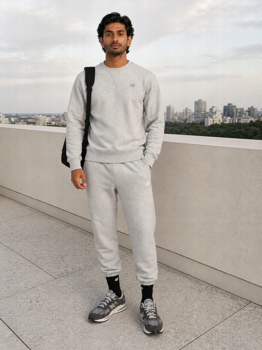 A tonal grey New Balance base keeps this combo clean, relaxed and quietly sporty, ideal for gym days, flights or laid-back city streets. The fleece crew and joggers read coordinated without feeling try-hard, while the grey runners and black technical duffel add just enough structure and function. Black ribbed socks tie it together, giving a small hit of polish in a still very casual frame.