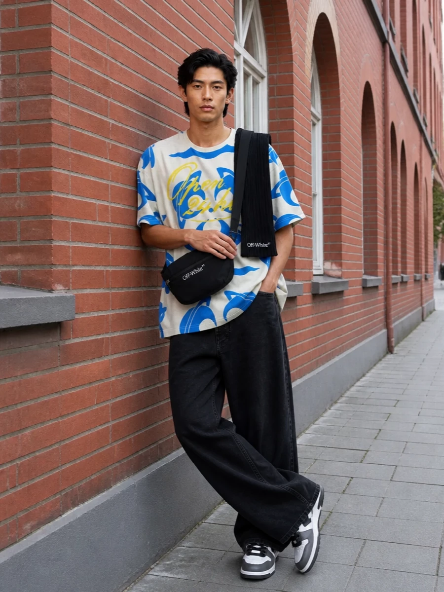 The Vivienne Westwood tee sits over washed black wide-leg denim for a graphic, laid-back streetwear take that lets the cobalt and yellow artwork stay front and center. Monochrome Off-White court sneakers and a streamlined belt bag echo the tee’s boldness in a tighter graphic language, keeping everything cohesive. A ribbed black scarf finishes the winter-ready attitude without stealing any focus from the statement top.