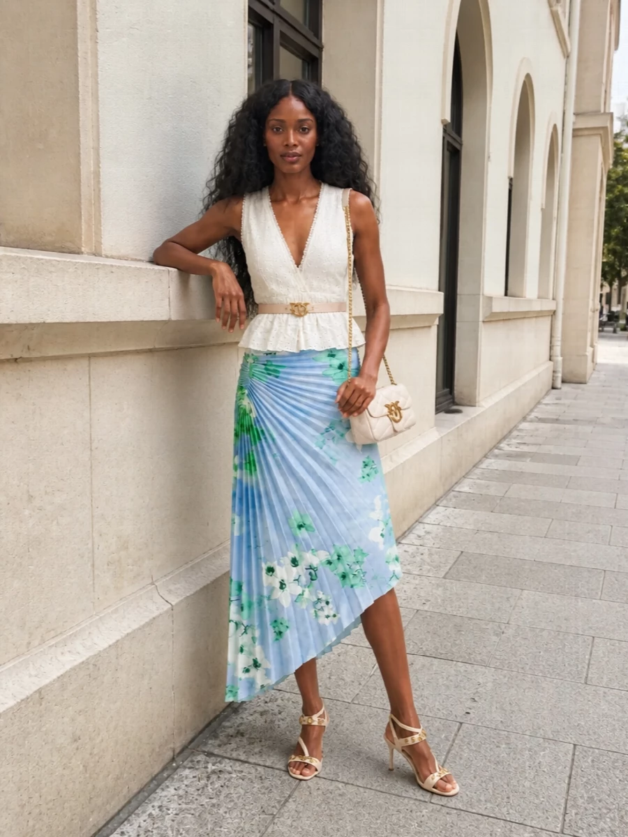 Romantic and light, this pairing lets the floral pleated skirt take center stage against a soft ivory peplum that neatly frames the waist. Cream, gold accented sandals and a matching quilted crossbody keep the palette airy and polished for spring terrace drinks or garden parties. A slim blush belt quietly ties the metallic notes together while keeping the silhouette feminine and defined.