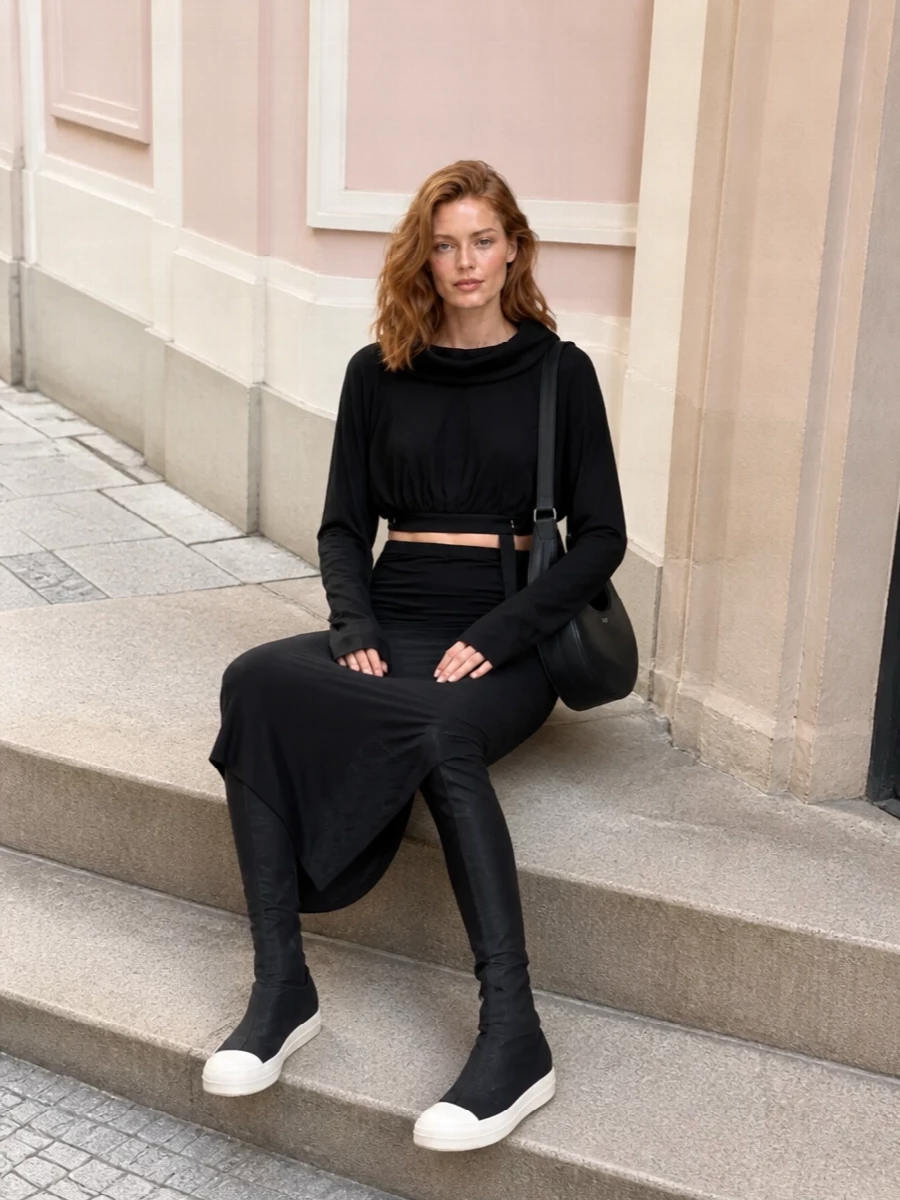 This look leans into a monochrome Rick Owens DRKSHDW mood: the cropped cocooned knit sits over a ruched black maxi skirt, creating a long, fluid column with just the right amount of offbeat structure. Over-the-knee sock boots extend the lines and add graphic contrast at the sole, while a sleek Coperni shoulder bag brings a subtle, sculptural counterpoint that keeps the outfit sharp for SS nights out or downtown days.