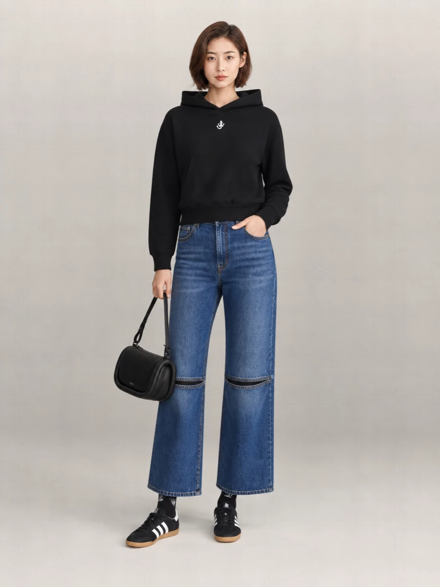 A cropped black JW Anderson knit hoodie meets structural wide-leg indigo denim for a clean, downtown uniform. Black and off-white sneakers and a sculpted black shoulder bag keep the palette tight while adding just enough polish. Logo socks peeking between hem and sneaker give a small, deliberate street detail without disturbing the minimalism.