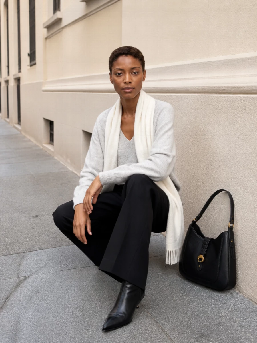A light heather grey V-neck knit meets relaxed black wide-leg tailoring for a quietly precise take on everyday dressing. Slouchy black ankle boots and a structured leather hobo keep the lines streamlined, while the ivory scarf softens the monochrome with just enough warmth. It is an easy, city-ready uniform that moves from office hours to dinner with minimal effort and maximum ease.