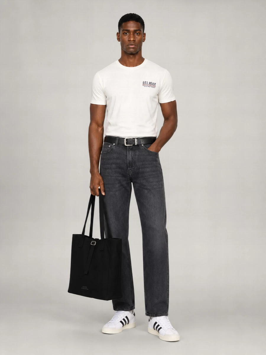 An off white logo tee sits against high-waisted washed-black denim for a clean, slightly graphic base that still feels relaxed. Classic white and black court sneakers keep it grounded in sport-influenced streetwear, while a structured black tote and slim belt sharpen the finish just enough for city days. The palette stays tight and neutral, letting the proportions and small branded details do the talking.