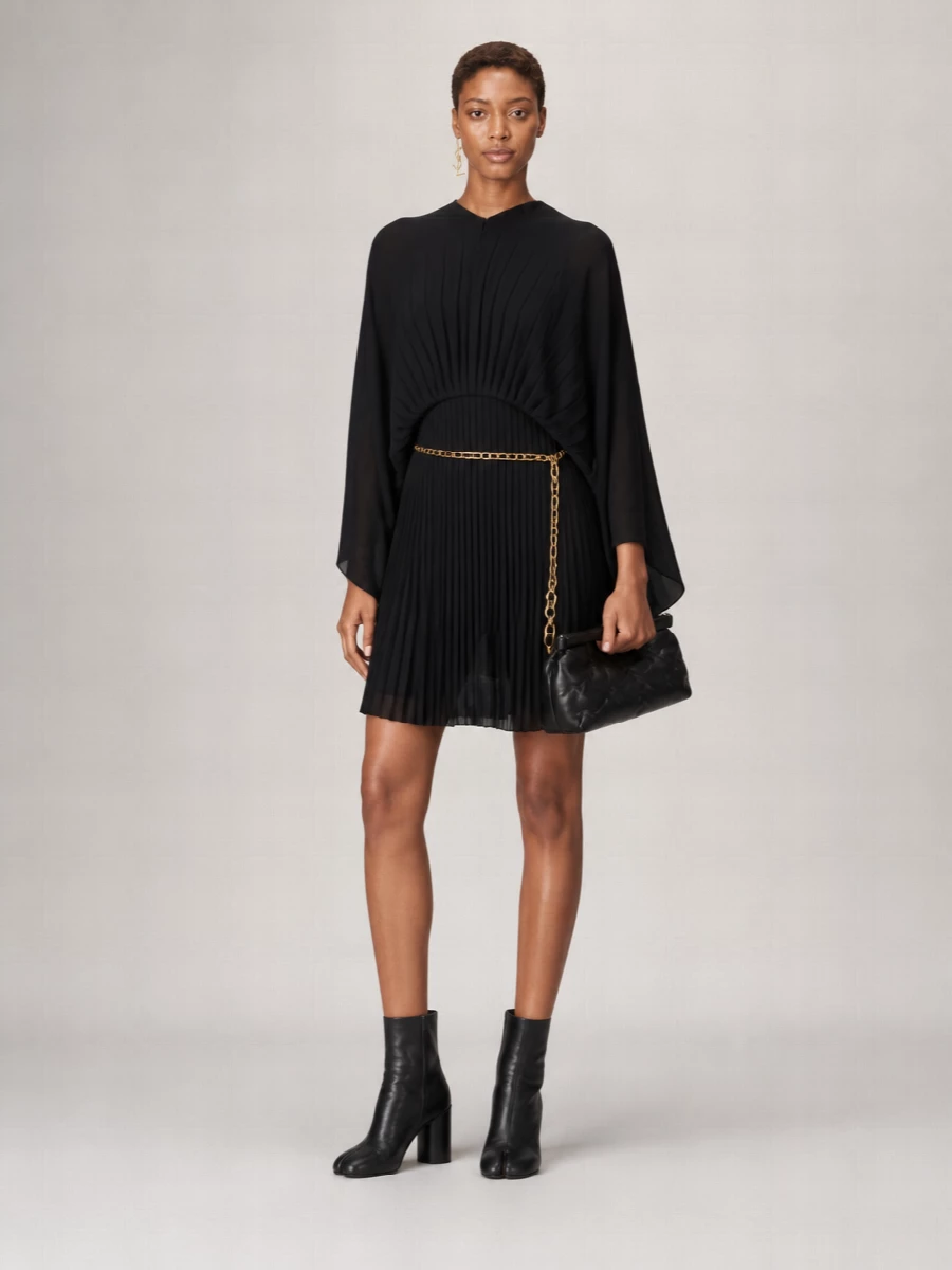 An all-black, sculptural Margiela ensemble that lets the pleated mini and cape do the talking, grounded by split-toe ankle boots for a quietly subversive line. A padded frame clutch and a single gold logo drop earring add just enough texture and light, while a fine chain at the waist gently shapes the volume without breaking the dress’s architectural flow.